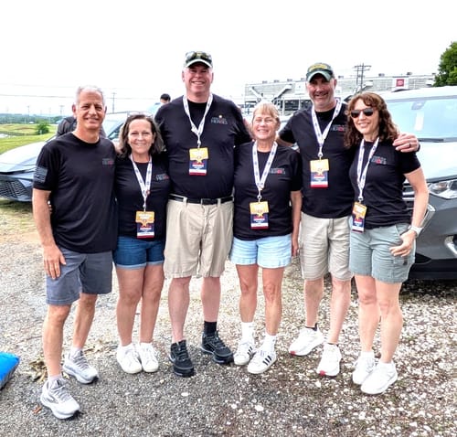 A group of six reviewers wearing matching black 'The Promise We Keep' tees at an outdoor event.