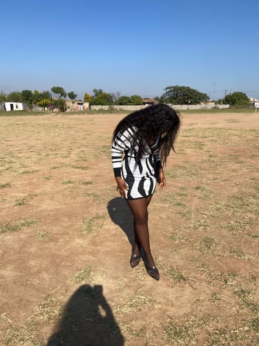 Customer standing outdoors in a field wearing the long-sleeved, black and white Striped V-Neck Mini Dress.