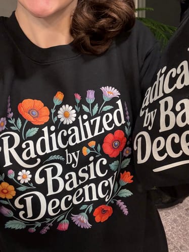 A customer wearing the black Radicalized By Basic Decency sweatshirt, showing the colorful floral graphic.