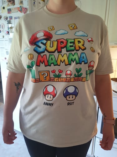 Eine Kundin trägt das personalisierte, beigefarbene "Super Mamma" T-Shirt im Videospiel-Stil.