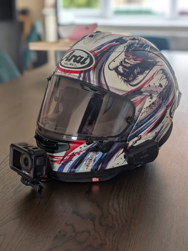 Customer's black Arai Camera Mount attached to the chin of a graphic helmet, holding a DJI action camera.