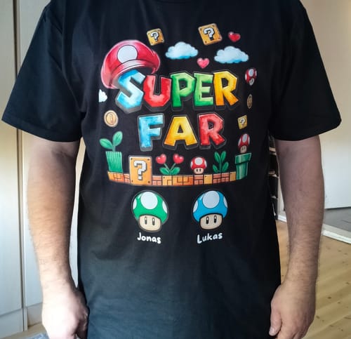 Anmelder iført en personlig sort 'Super Far' t-shirt med spil-tema og navnene 'Jonas' og 'Lukas'.