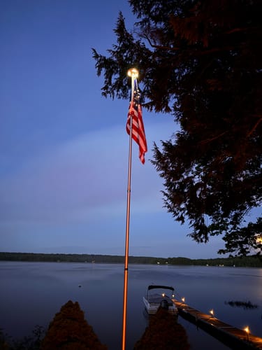 Reviewer's Betsy Ross Flag flying on an illuminated flagpole at dusk over a lake.