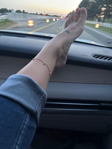 Reviewer wearing the delicate gold Vera Anklet while resting their foot on a car's dashboard.