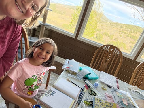 Reviewer and a child smiling over a table with planners and stickers from the Ultimate Subscription.