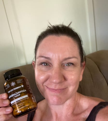Customer smiling while holding a brown bottle of Organic Ashwagandha Capsules.
