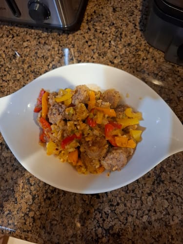 Customer's prepared dish of Mild Italian Sausages, cut into pieces and mixed with colorful peppers in a white bowl.