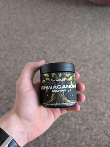 Customer holding a black bottle of Ashwagandha KSM-66 in their hand against a carpeted background.