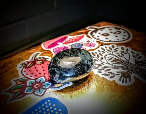 Customer's polished dark monthly crystal with a white marking, shown close-up on a sticker-covered surface.