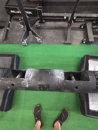 Customer wearing black Vitality III barefoot shoes in a gym, standing before a strongman log.