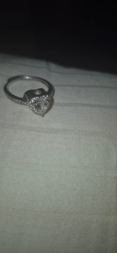 Close-up of a reviewer's silver-colored, heart-shaped urn ring on a light surface.