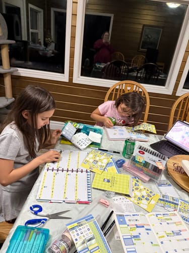 Customer's children using colorful stickers and planners from the Ultimate Subscription box at a table.
