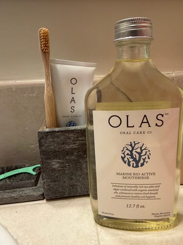 Reviewer's OLAS Marine Sea Mint Toothpaste in a stone holder on a bathroom counter, next to the brand's mouthrinse.