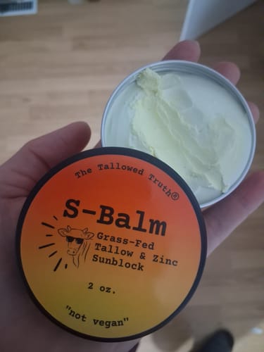 Customer holding an open tin of S-Balm Tallow and Zinc Sun Lotion, revealing the creamy product inside.