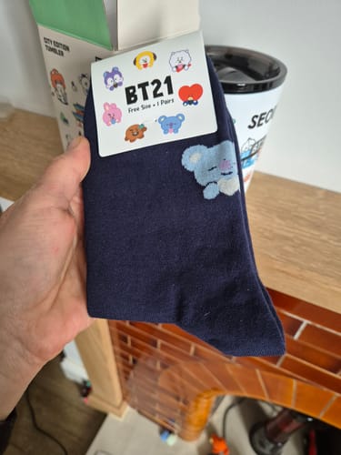 Customer holding up a new pair of navy BT21 socks with the packaging attached.