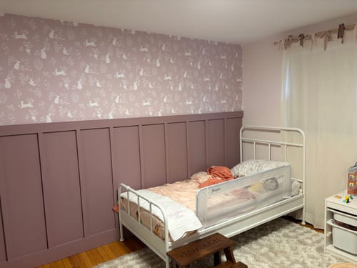 Customer's Aven Wallpaper with a delicate animal pattern installed above mauve wainscoting in a bedroom.