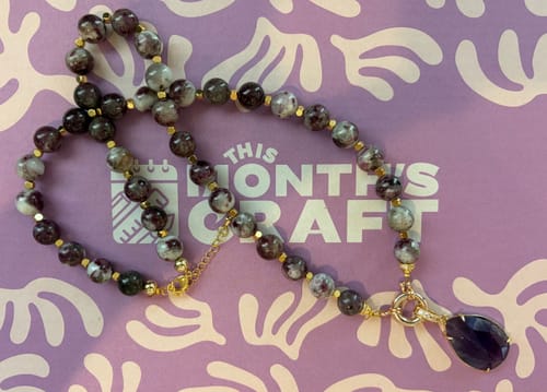 Reviewer's beaded necklace with a purple pendant, made from the craft subscription box.