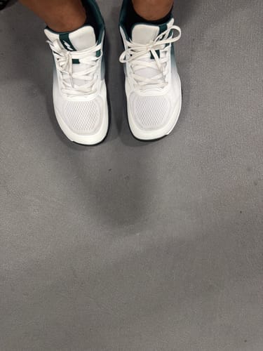 A top-down view of a customer wearing white CUURT Muuv wide toe box court shoes on a gray floor.