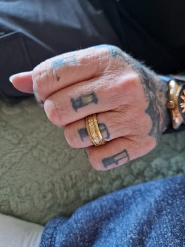 A close-up of a customer's tattooed hand wearing the gold and textured Aureum ring.