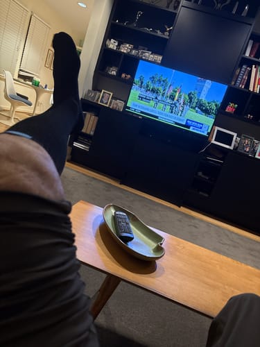 Reviewer relaxing with their foot up, wearing a black Performance Eucalyptus Compression Sock in their living room.