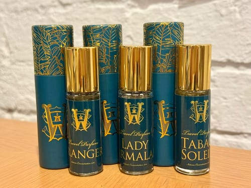 Reviewer's three Bag Size for Travel perfumes shown with their decorative teal and gold cylindrical packaging.