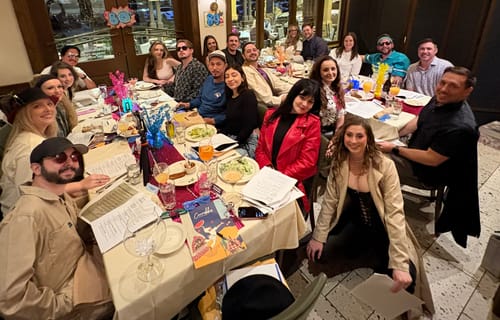 Customers in 80s costumes playing the Murder Mystery Game Kit around a long decorated table.