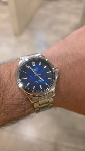 Cliente mostrando su reloj Casio Sapphire con esfera azul y pulsera de acero en la muñeca.