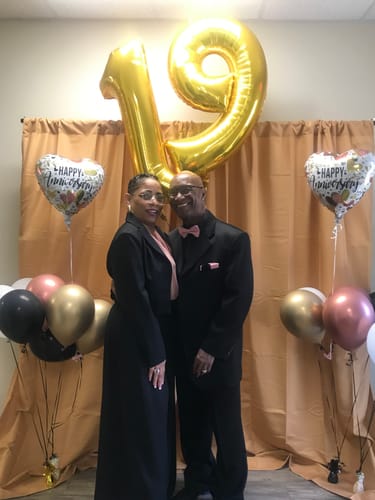 Reviewer posing with a partner in a black Notched Collar Blazer and matching pants at a celebration.