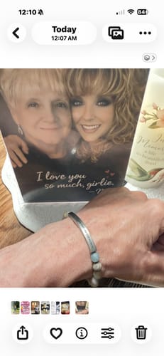 Close-up of a reviewer wearing the 'BE STILL' engraved bracelet on their wrist in front of a sentimental photo.