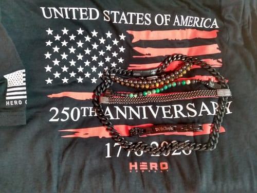 Customer's black Never Retreat Alpha Wolf Cuban Link Necklace displayed with other bracelets on a patriotic t-shirt.
