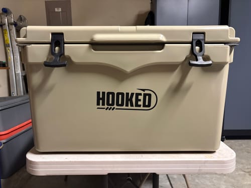 Customer's tan Hooked 50 cooler on a small table, highlighting the slightly crooked front logo decal.