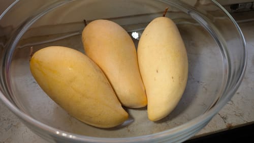 Ein Kunde zeigt drei reife, gelbe Nam Dok Mai Mangos in einer Glasschüssel.