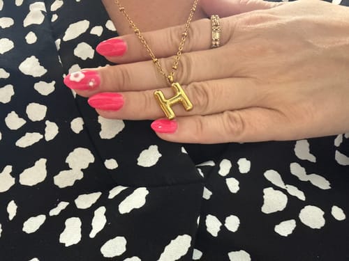 Customer's hand holding up their gold Bubble Letter Initial 'H' Necklace against a patterned top.