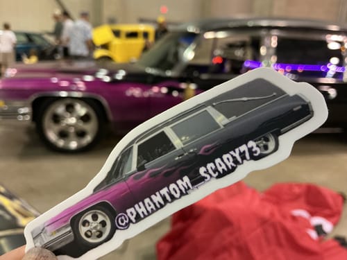 Customer holding a custom vinyl sticker of their purple hearse, with the real car in the background.
