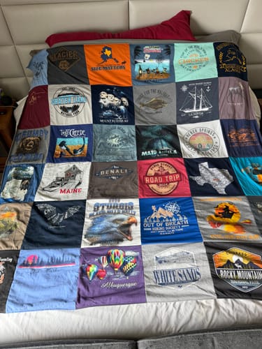 Customer's colorful Project Repat T-Shirt Quilt, made from many travel shirts, spread neatly on a bed.