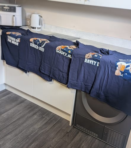 Customer's five custom-printed Men's heavyweight t-shirts for a stag do, lined up on a counter.
