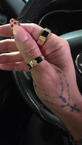 Close-up of a customer's hand wearing the Gold Crystal Clover Band Ring on their thumb inside a car.