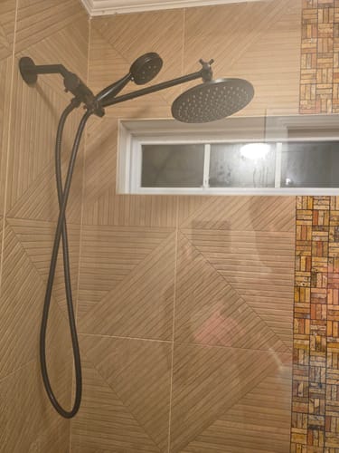 Reviewer's dark metal Dual Shower Head installed in a tiled shower, showing both heads extended.
