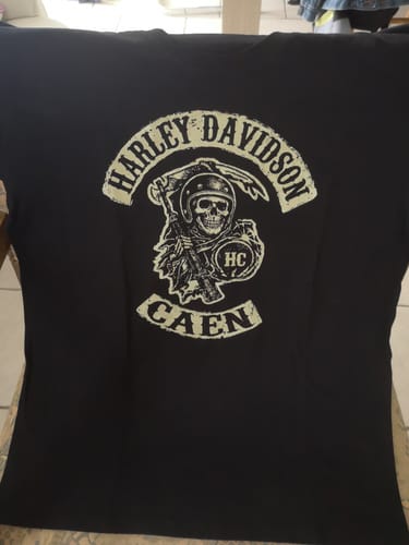 Client présentant le T-shirt noir Faucheuse HC à plat, avec un logo de faucheuse motarde.