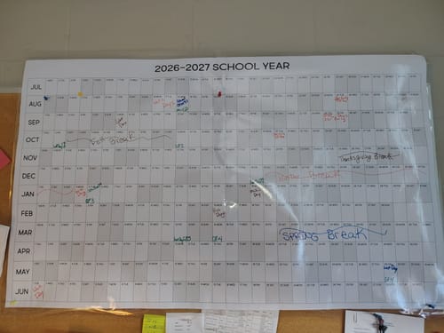 Reviewer's laminated 2026-27 School Year Calendar on a wall, marked with handwritten dates and events.