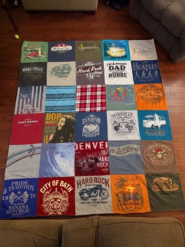 Reviewer's finished Project Repat T-Shirt Quilt, made from a collage of memorable t-shirts, laid on a floor.