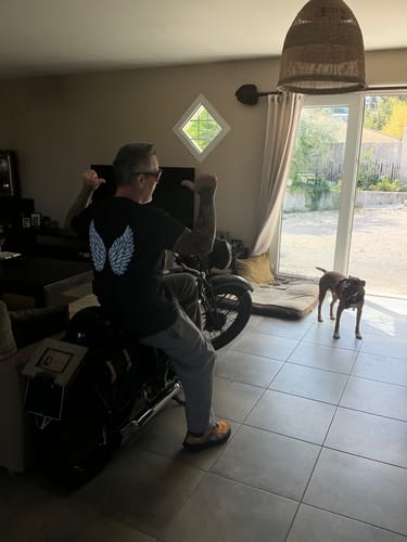 Client montrant le dos de son T-Shirt Ange noir avec des ailes, assis sur une moto à l'intérieur.