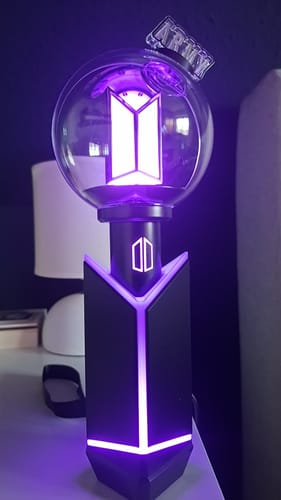 Reviewer's BTS Official Light Stick Ver.4 in its cradle, glowing with a bright purple light on a desk.