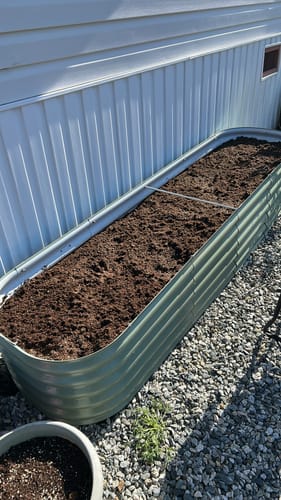 Reviewer's long, green modular garden bed filled with soil and set up next to a house.