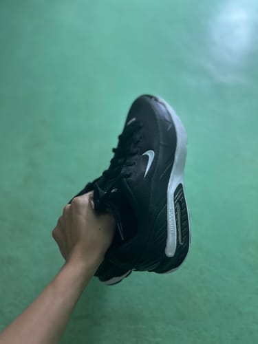 A customer's hand holding a single black Nike Air Max Bia Casual Shoe, showing the side profile and white sole.