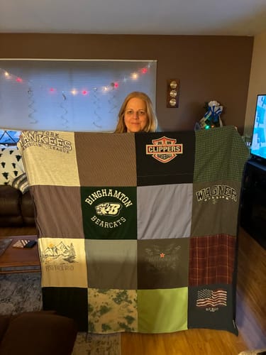 Customer holding up their new Premium T Shirt Quilt, showing various t-shirt squares with sports and college logos.