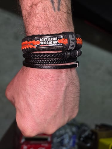 Customer's wrist showing the black and orange Hard Days - Paracord Bracelet stacked with other bracelets.
