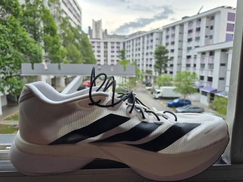 Customer's white adidas Adizero Boston 13 running shoe resting on a windowsill, showing its side profile.