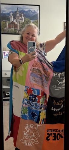 Reviewer taking a mirror selfie while wrapped in their colorful Project Repat T-Shirt Quilt.