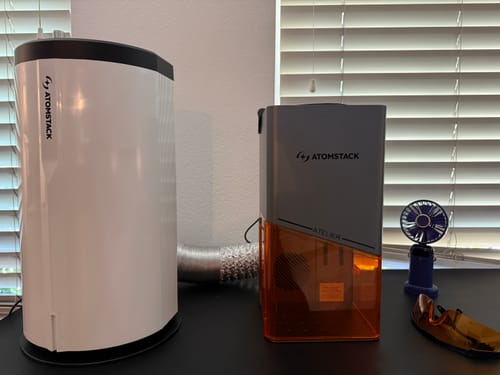 Reviewer's grey AtomStack Atelier laser engraver with its orange safety shield set up on a desk.